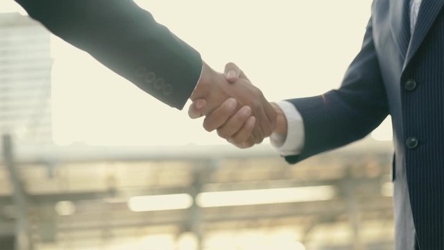 Asian businessman and businesswoman shaking hands partnership deal business while standing outside on the street near a big office building urban in the morning.
