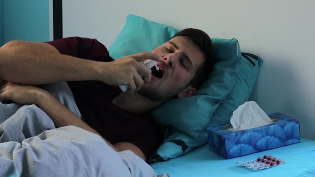 Young Sick man Coughing In Bed And Using Throat Spray - Medium Shot

