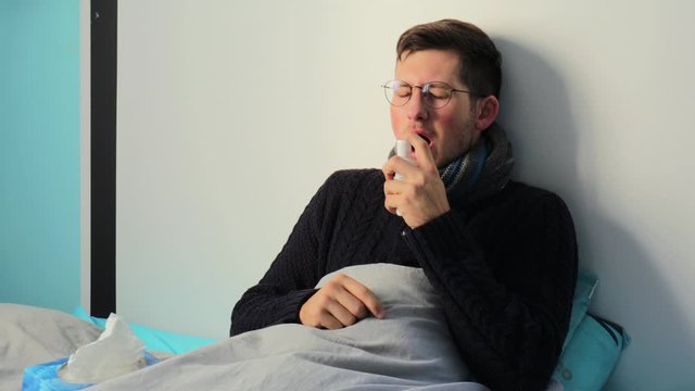 A Man Sick At Home, Coughing And Blowing His Nose And Taking Throat Spray  - Medium Shot