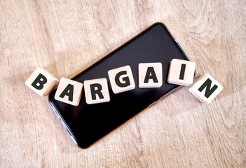 Text bargain on wooden cubes on a black smartphone. Cubes lay on a black smartphone on the wooden...