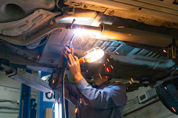 A welder in a car service repairs a car raised on a lift