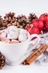 Cup of hot chocolate with marshmallows, and some cinnamon sticks, cones, christmas balls and candles	