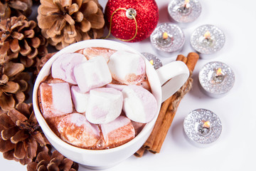 Cup of hot chocolate with marshmallows, and some cinnamon sticks, cones, christmas balls and candles	