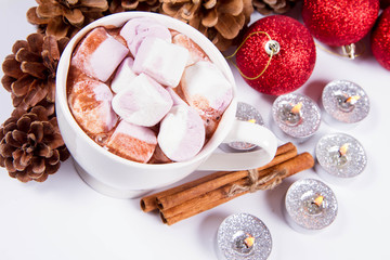 Cup of hot chocolate with marshmallows, and some cinnamon sticks, cones, christmas balls and candles	