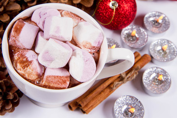 Cup of hot chocolate with marshmallows, and some cinnamon sticks, cones, christmas balls and candles	