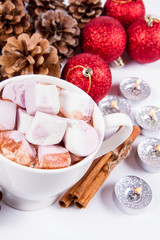 Cup of hot chocolate with marshmallows, and some cinnamon sticks, cones, christmas balls and candles	