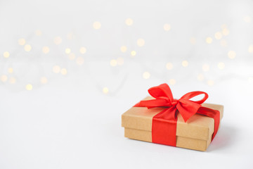 Gift box with a red bow on a background of blurred lights garland. Christmas background.
