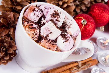 Cup of hot chocolate with marshmallows, and some cinnamon sticks, cones, christmas balls and candles	