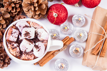 Cup of hot chocolate with marshmallows, and some cinnamon sticks, cones, christmas balls, candles and a gift	