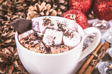 Cup of hot chocolate with marshmallows, and some cinnamon sticks, cones, christmas balls and candles	