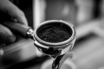 A black and white close up portrait of a portafilter full of coffee grounds from freshly grinded coffee beans.