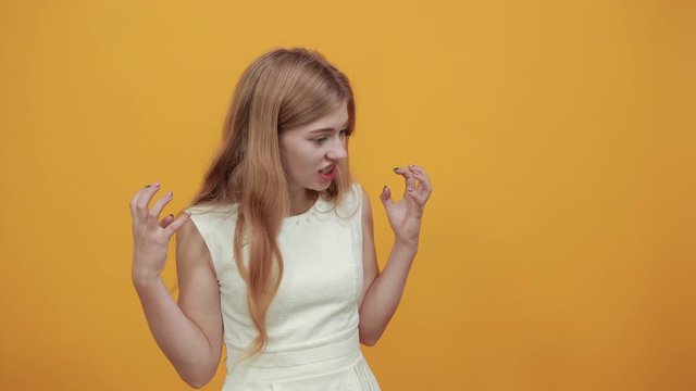 Disappointed caucasian young lady doing anmal agressive gesture over isolated orange background wearing white shirt. Lifestyle concept