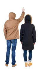 Back view of couple couple in winter jackets pointing.