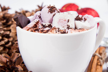 Cup of hot chocolate with marshmallows, and some cinnamon sticks, cones, christmas balls and candles	