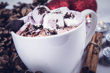 Cup of hot chocolate with marshmallows, and some cinnamon sticks, cones, christmas balls and candles	