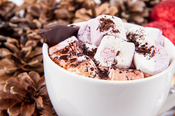 Cup of hot chocolate with marshmallows, and some cinnamon sticks, cones, christmas balls and candles	