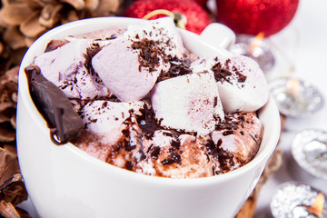 Cup of hot chocolate with marshmallows, and some cinnamon sticks, cones, christmas balls and candles	