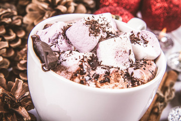 Cup of hot chocolate with marshmallows, and some cinnamon sticks, cones, christmas balls and candles	