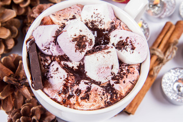 Cup of hot chocolate with marshmallows, and some cinnamon sticks, cones, christmas balls and candles	