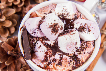 Cup of hot chocolate with marshmallows, and some cinnamon sticks, cones, christmas balls and candles	