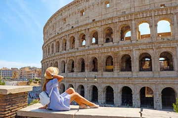 Papier Peint photo Rome Femme de voyage en robe romantique et chapeau assis et regardant le Colisée, Rome, Italie. Belle fille touristique avec sac à dos près du Colisée. Une jeune femme profite des vacances d& 39 été italiennes en Europe.