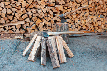 Dry oak firewood stacked in a pile, chopped wood for winter heating of the fireplace. An ax and a deck for chopping wood. Natural wood background.