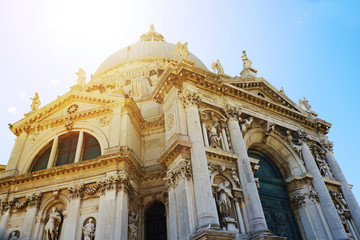 Fototapeta na wymiar Beautiful view of famous Basilica di Santa Maria della Salute in warm sunset light with sunbeams in Venice, Italy. Cathedral on Grand Canal, old Italian architecture in sunlight with sun rays.