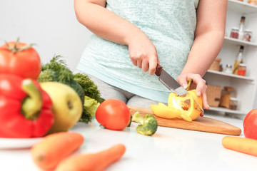 Obraz na płótnie Canvas Body Care. Chubby girl standing in kitchen cutting vegetables for dinner cllose-up