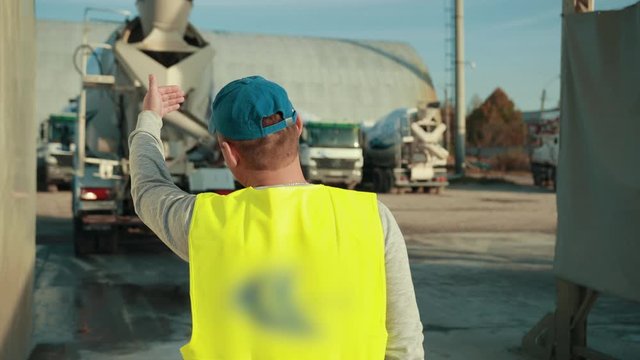 Worker is indicating something to truck driver. Worker is directing him to come to his desired direction or location as this is his job to instruct the truck driver.