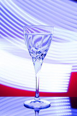 A glass with a drink on a red background with abstract blue light lines, on a black glossy table. The concept of the holiday, new year.