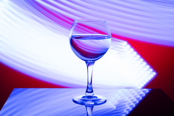 A glass with a drink on a red background with abstract blue light lines, on a black glossy table. The concept of the holiday, new year.