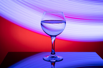 A glass with a drink on a red background with abstract blue light lines, on a black glossy table. The concept of the holiday, new year.