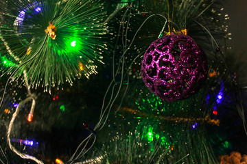Obraz na płótnie Canvas Christmas tree branch with purple ball in close up. New year decorations on a background of a greenfir tree with a bright garland and plastic toys.