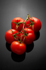 Image of fresh tomatoes bunch on black background with reflection and water drops