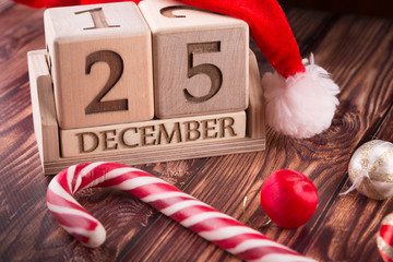 Wooden cube calendar with 25 december date staying on table near different holiday decorations. Christmas composition.