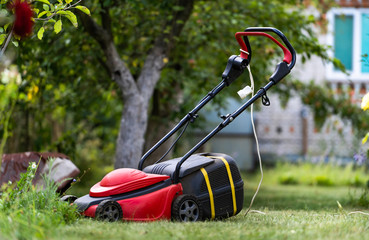 Lawn mower on a lawn in the garden, gardening. Red machine with tank for grass. Gardening concept.