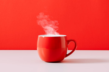 Steaming coffee cup on red background. Red сoffee cup with steam. Front view, copy space