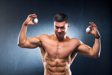 Men holding two white eggs on a grey background. Bodybuilder with eggs, naked torso. Healthy...