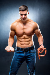Fototapeta na wymiar Muscular young sportsman holding chicken breasts and sausage. Dieting and sport nutrition, naked torso, athletic man. Closeup