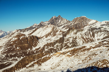 Beautiful nature landscape of Swiss Alps in sunlight rays. Sunset mountains covered with snow in Switzerland. Great view of the snowy rocks and sun beams in Alpine ski resort. Winter holidays.