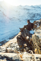 Traveler Man with backpack trekking in mountains, enjoy beautiful Matterhorn view. Explorer man hiking on snowy hills, travel in Alps, Switzerland. Hiker sitting on rock cliff outdoors on nature.