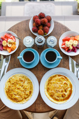 Top view, table setting. Balinese tropical breakfast of fruit, coffee and scrambled eggs and banana pancake for two. on the street near the pool