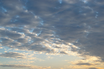 Rows of flattened small clouds float slowly across the sky, illuminated by the yellow rays of the setting sun