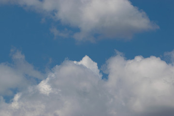 The top of a huge white cumulus cloud against a blue sky partially overlapped by another cloud