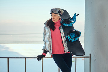 Obraz premium Young active woman with snowboard is posing for photographer at bright winter day.
