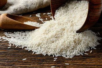Uncooked long rice heap spilled out from the bowl on wooden table.