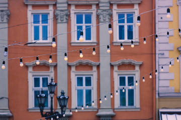 Fototapeta na wymiar Garlands with bulbs on the background of blue windows of buildings and a street lamp in the center of a European city. Christmas fabulous atmosphere on Market Square in Lviv, Ukraine