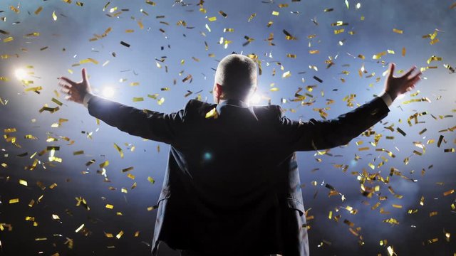 Successful businessman with arms up celebrating his victory. Celebrating success. Low angle view of excited young businessman keeping arms raised and expressing positivity while stands on the stage.