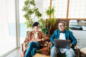 Two male Japanese professionals working on laptop computers in a co-working space.