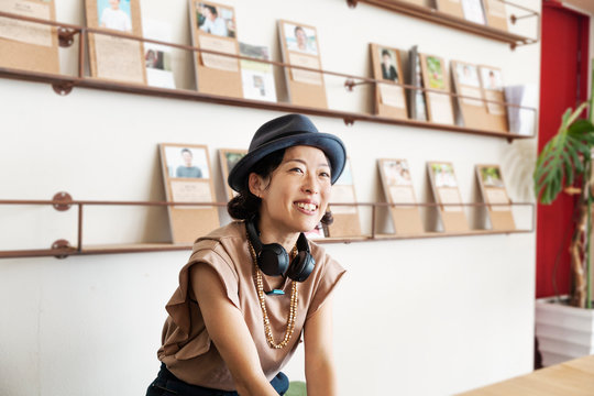 Female Japanese professional wearing Trilby hat and headphones sitting  in a co-working space.